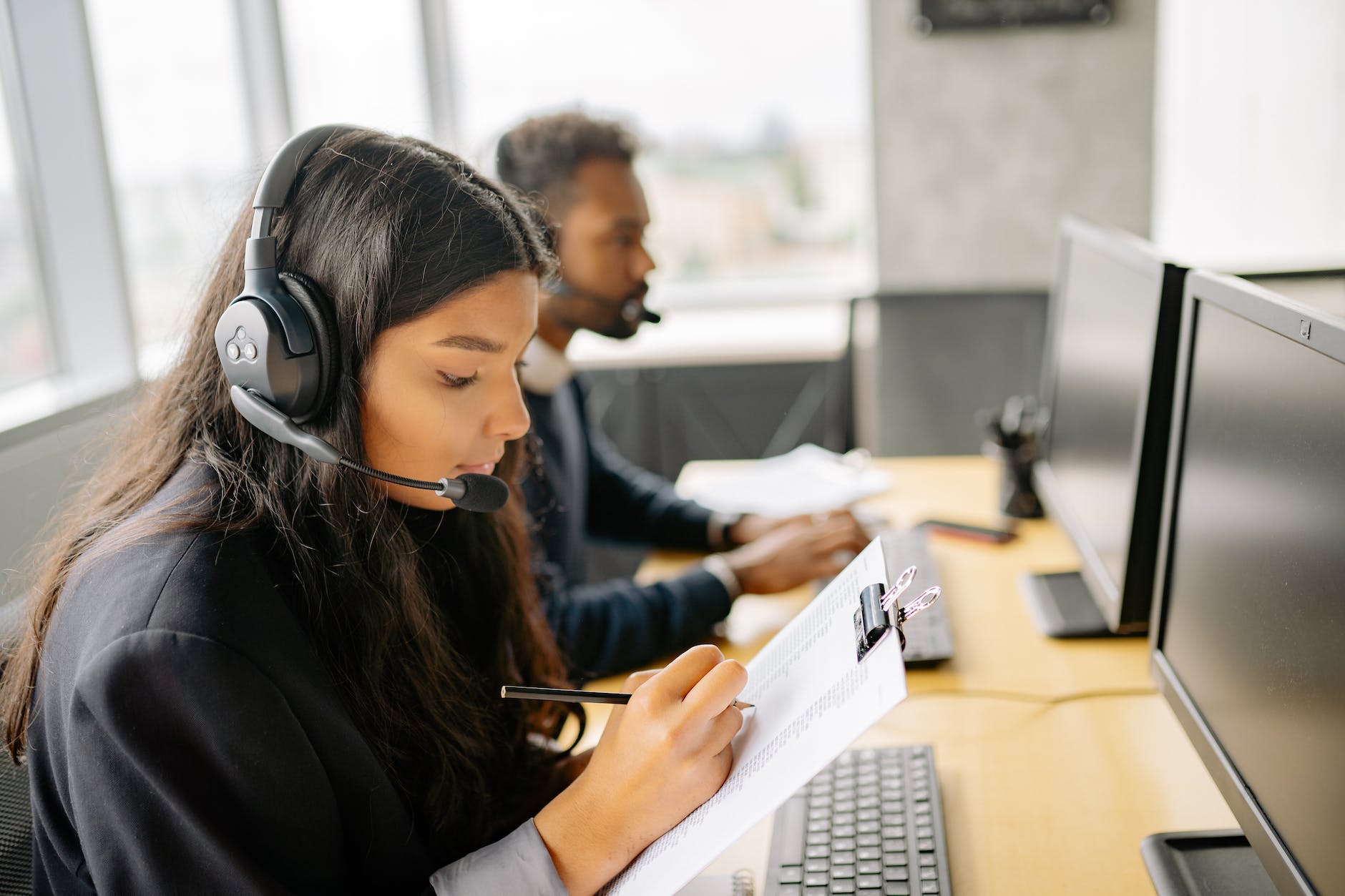 woman with headset holding a clipboard and taking notes